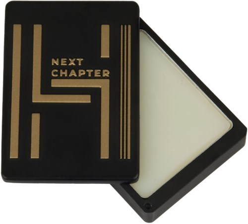En svart låda med gyllene linjer och text som säger "Next Chapter" inuti, med en vit yta under.