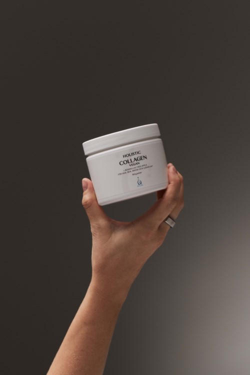 En hand håller en vit burk märkt 'Hyaluronic Collagen'. Bakgrunden är mörk och enkel.