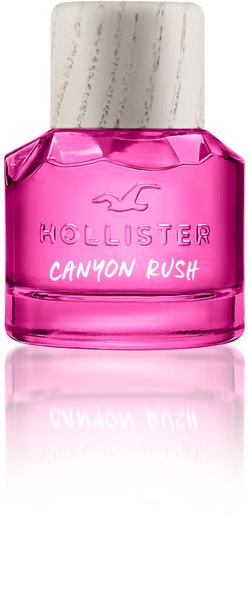 Een klein roze parfumflesje met witte dop, gelabeld Hollister Canyon Rush, weerkaatst op een glanzend oppervlak.