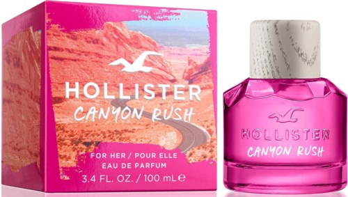 Roze en witte doos met woestijnlandschap, roze parfumfles met witte dop, Hollister-logo en tekst, productnaam.