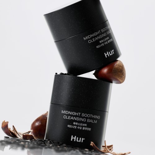 Zwei schwarze Tiegel mit Hautpflegebalsam, Holzapplikator und braune Dekorationen.