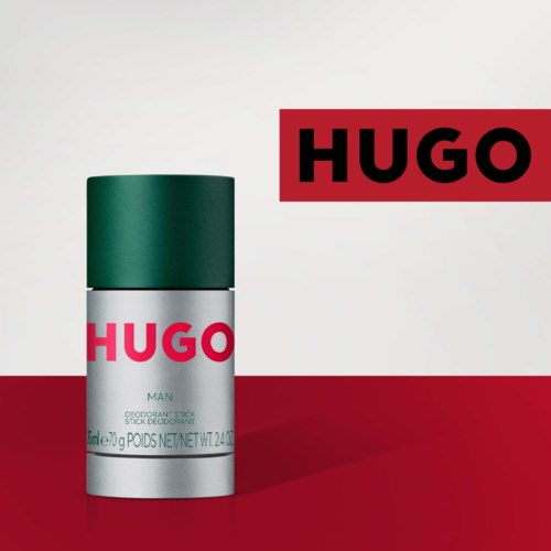 Een deodorant spray met een groene dop en een label met 'HUGO' staat op een rode en grijze achtergrond.