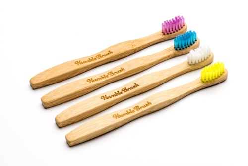 Four wooden toothbrushes with different colored brush heads: pink, blue, white, yellow.