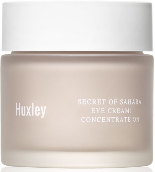 Een beige pot met witte deksel, met label 'Huxley' en 'Secret of Sahara Eye Cream: Concentrate On.'