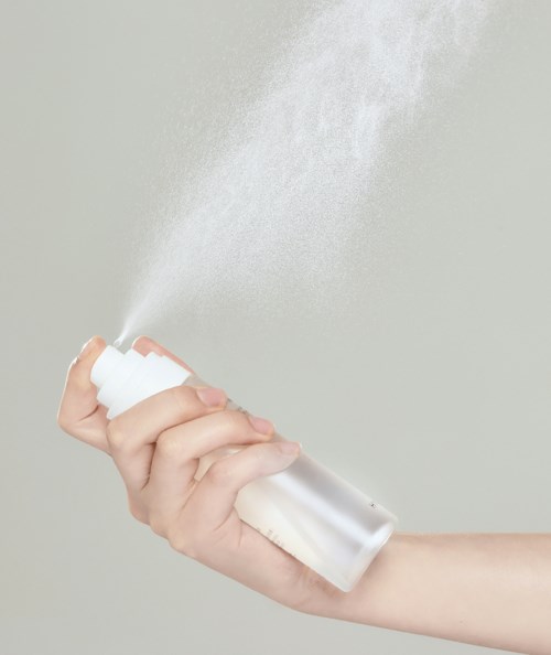 A hand sprays a fine mist from a white aerosol can.