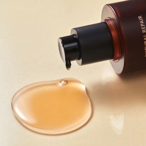 A bottle labeled 'Natural Repair' with a drop of liquid on a beige surface.