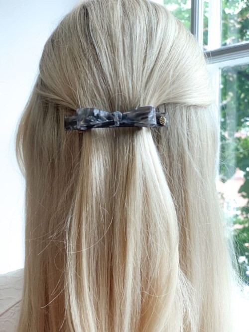 Blonde hair tied with a black and white patterned bow, viewed from behind by a window.