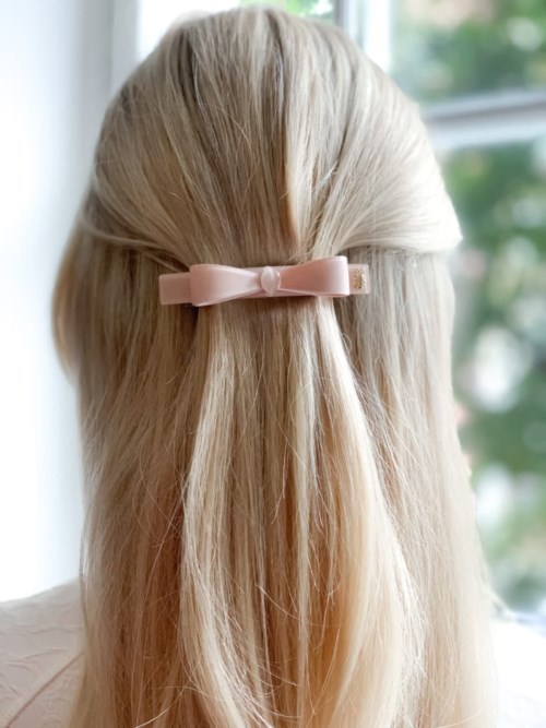 Blonde hair tied with a pink bow woman looking out a window.