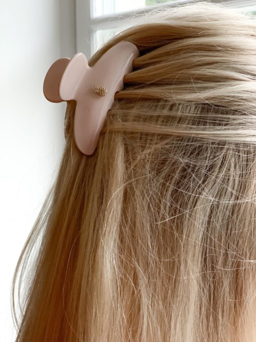 A beige hair clip is attached to blonde hair near the scalp, parting the hair to the side.