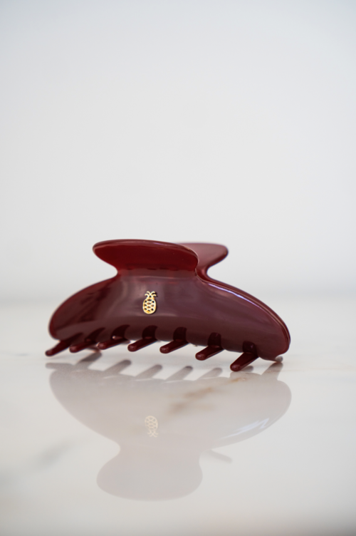 A red hair claw clip with a small gold pineapple charm on it, placed on a white surface.
