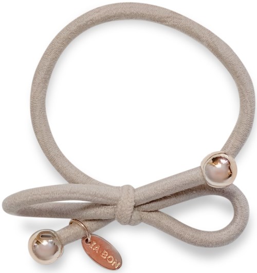 A beige fabric hair tie with a bow and two pearl and gold accents.