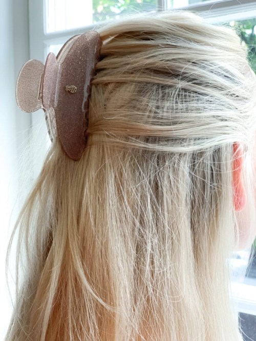A girl has a large, glittery hair clip in her blonde hair by a window. She is facing away from the camera.
