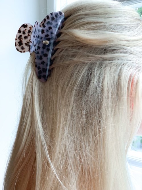 A girl with long blonde hair wears a leopard print hair clip with bear ears. She is near a window.