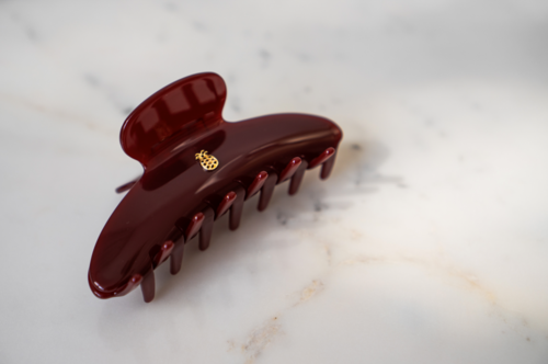 A maroon hair clip with a small decorative gold-like charm on top, placed on a white surface.