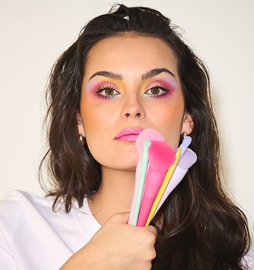 Woman with colorful makeup holding several pastel-colored spatulas.
