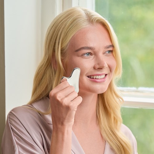Nainen, jolla on blondeja hiuksia, hymyilee ja puhuu valkoisella langattomalla puhelimella ikkunan lähellä.