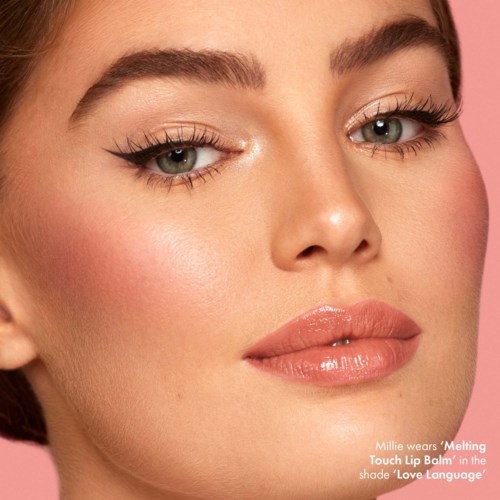 Close-up of a woman with bright makeup, bold eyeliner, and glossy lips. She has fair skin and light eyebrows.
