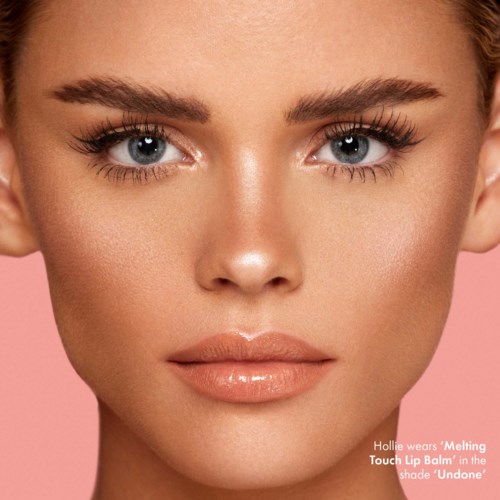 Close-up of a woman with bright eyes, smooth skin, and glossy lips, against a pink background.