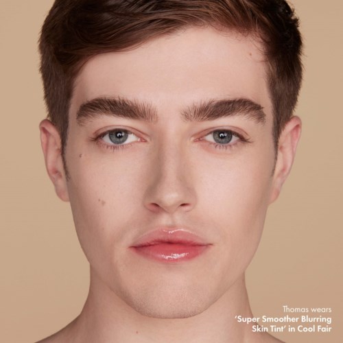 A young man with fair skin, light features, and styled short brown hair, posing against a beige background.