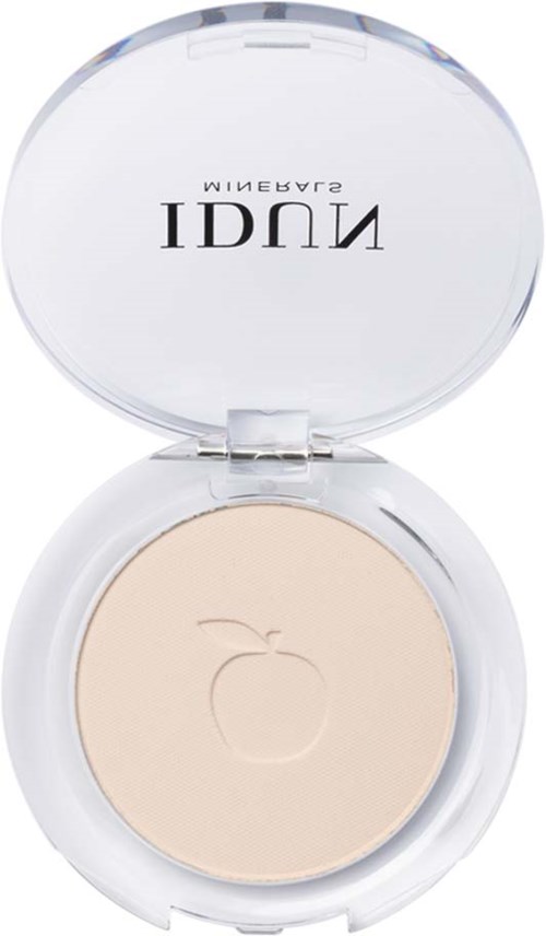 A compact with a beige powder and a clear, round lid that has black text on it.