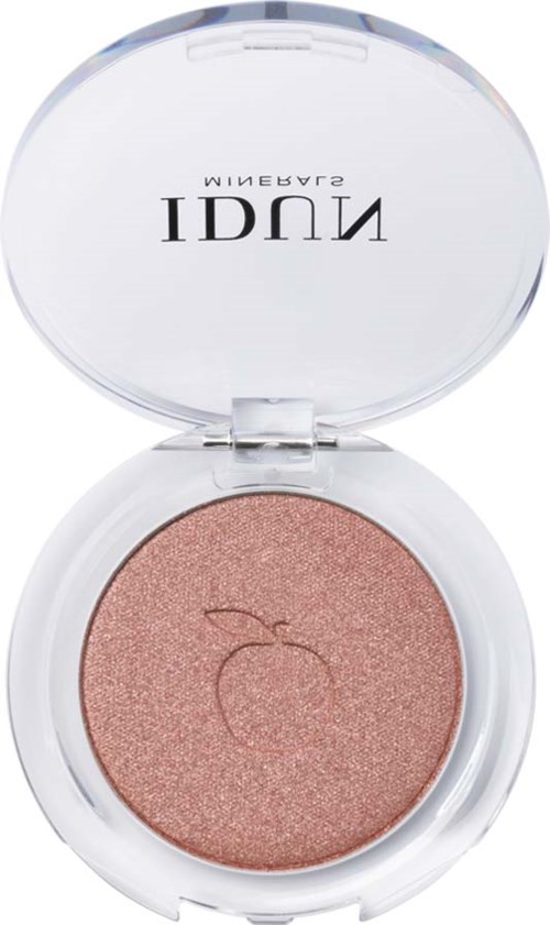 A compact with shimmery peach-colored makeup, a small leaf symbol, and a clear lid with text upside down.