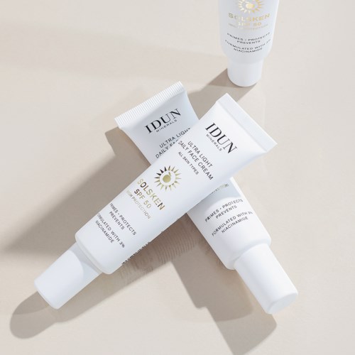Three white tubes of face cream or sunscreen with black text and a small sun logo on a beige surface.