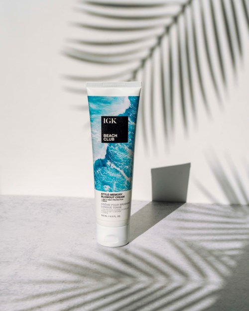 Eine Tube IGK Beach Club Smoothing Blowout Cream vor hellem Hintergrund mit Schatten von Palmblättern.