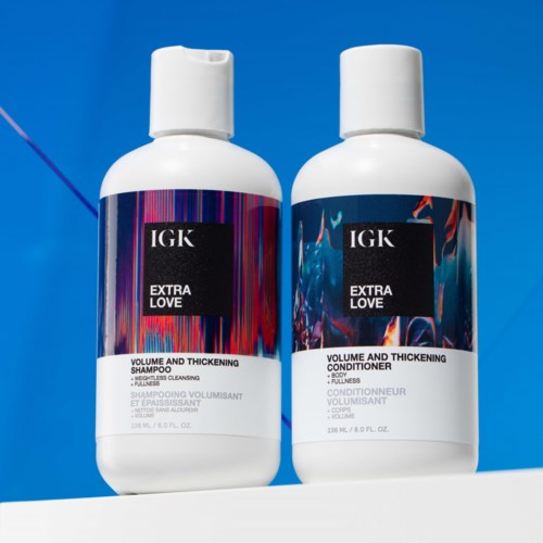 Zwei Flaschen Haarpflegeprodukte: Shampoo und Conditioner, von IGK's Extra Love Linie, auf blauem Hintergrund.