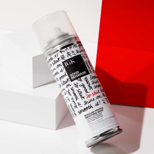 Eine Dose IGK Good Behavior Glättungsspray, schwarz-weiß-rot gestaltet, auf weißen Plattformen mit rotem Hintergrund.