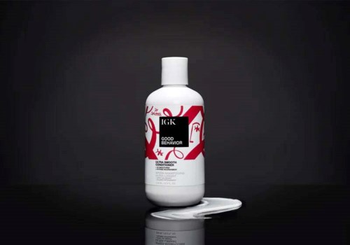 Een witte fles met zwart en rood label, ligt op een donkere oppervlakte, met wat vloeistof ernaast.
