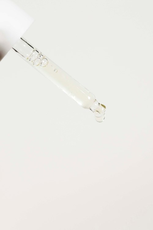 Een pipet legt een heldere vloeistof met bellen neer op een witte achtergrond.