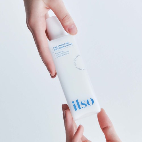 Een hand houdt een witte fles met het label "ilso" die dagelijkse vochtinbrengende en verzachtende lotion beschrijft.