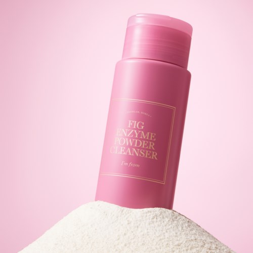 En rosa flaske merket 'Fig Enzyme Powder Cleanser' står på pulver med rosa bakgrunn.