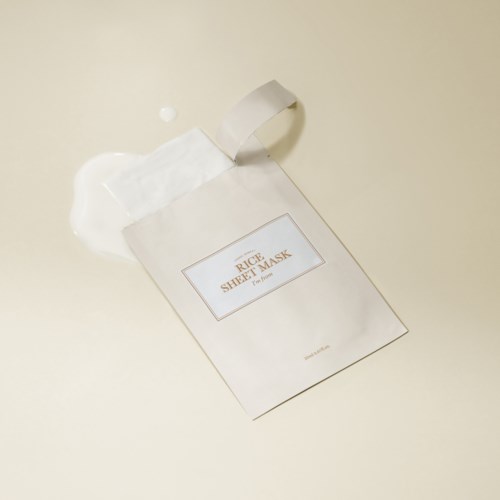 Een wit sheetmasker ligt op een lichte ondergrond met wat vloeistof die ernaast is gemorst.