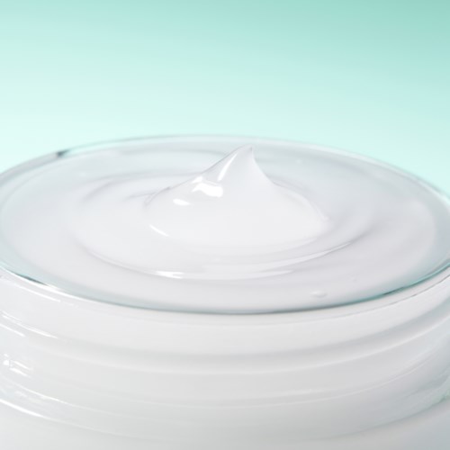 Et nærbilde av hvit krem eller lotion i et glasskrukke mot en lys bakgrunn.