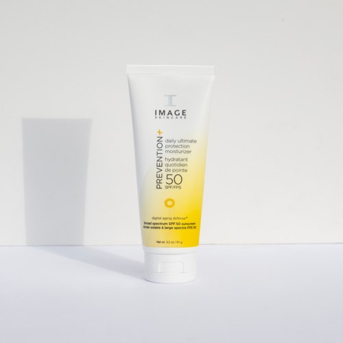 En vit tub med solskyddsmedel med SPF 50 står på en vit yta. Etiketten har gul och svart text.