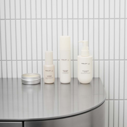 Four white skincare bottles and a silver container on a rounded gray surface against a white tiled wall.