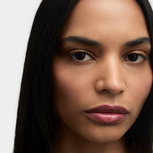 A close-up of a woman with straight dark hair and natural makeup against a light background.