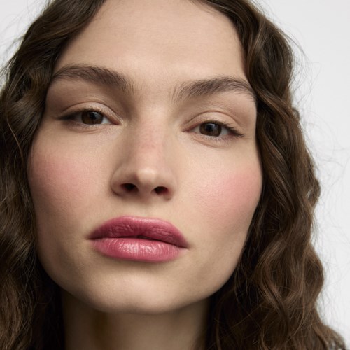 A close-up of a woman with wavy brown hair, natural makeup, and pink lips, looking at the camera.