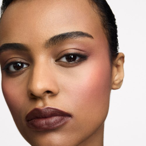 Nahaufnahme einer Frau mit makelloser Haut, dunklem Haar und neutralem Make-up, schaut in die Kamera.