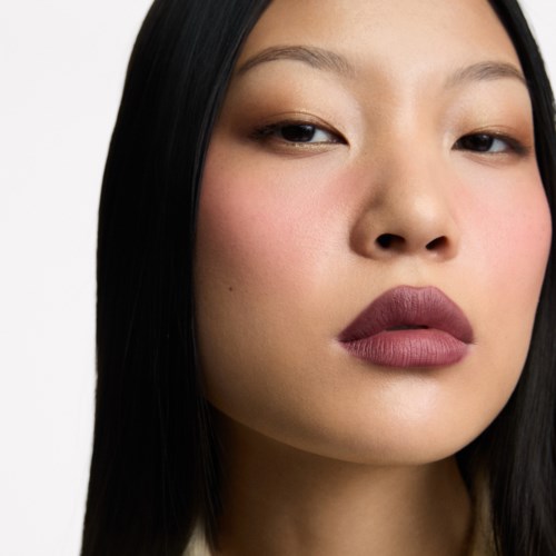 Nahaufnahme einer Frau mit langen schwarzen Haaren, leicht geschlossenen Augen und mattem Lippenstift.