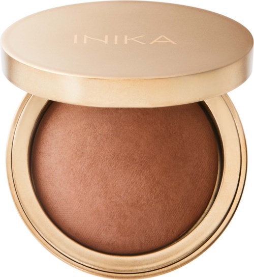 Pyöreä kompakti, jossa beige kansi ja merkki 'INIKA'. Sisällä on ruskea puuteri.