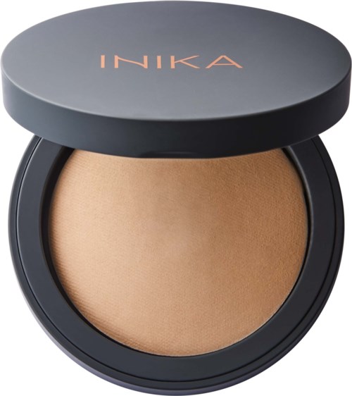 A compact makeup product with beige powder inside and a gray lid with 'INKA' written on it.