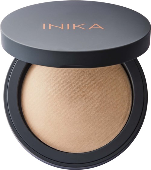 A round compact with beige powder inside and a black lid with rose gold text 'INIKA'.