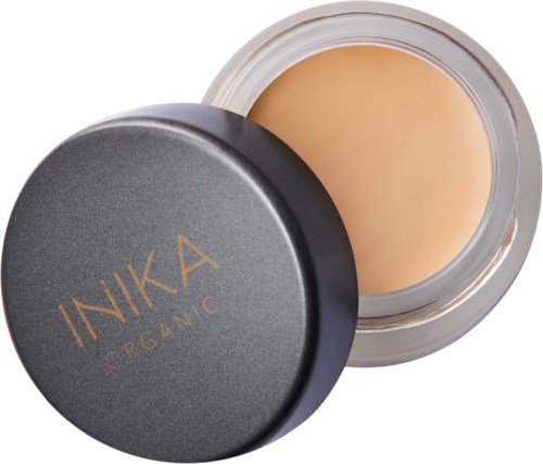 A small round container with a black lid labeled 'INIKA ORGANIC' contains beige cream or foundation.