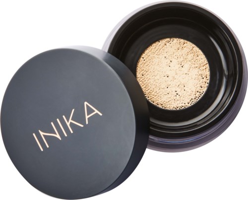 A black container with the brand name INIKA on the lid, opened to show beige powder inside.