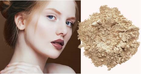 A woman with light makeup and dark lipstick faces sideways next to a pile of beige powder.