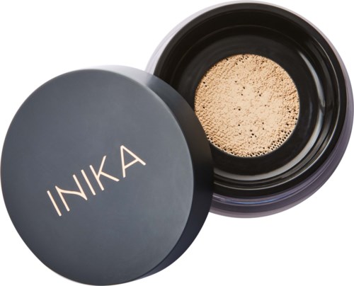 A black round container with a lid labeled 'INIKA'. The lid is off, showing a beige powder inside.