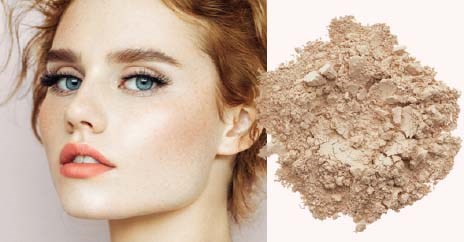 A woman with clear skin and blue eyes next to a pile of loose face powder.