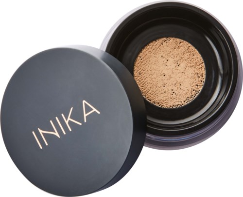 A black container with a lid labeled 'INIKA' shows loose powder inside. The lid is tilted open, revealing powder.